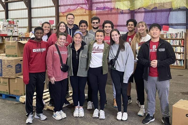 15 students stand together in front of boxes full of donated books at a book drive volunteer event