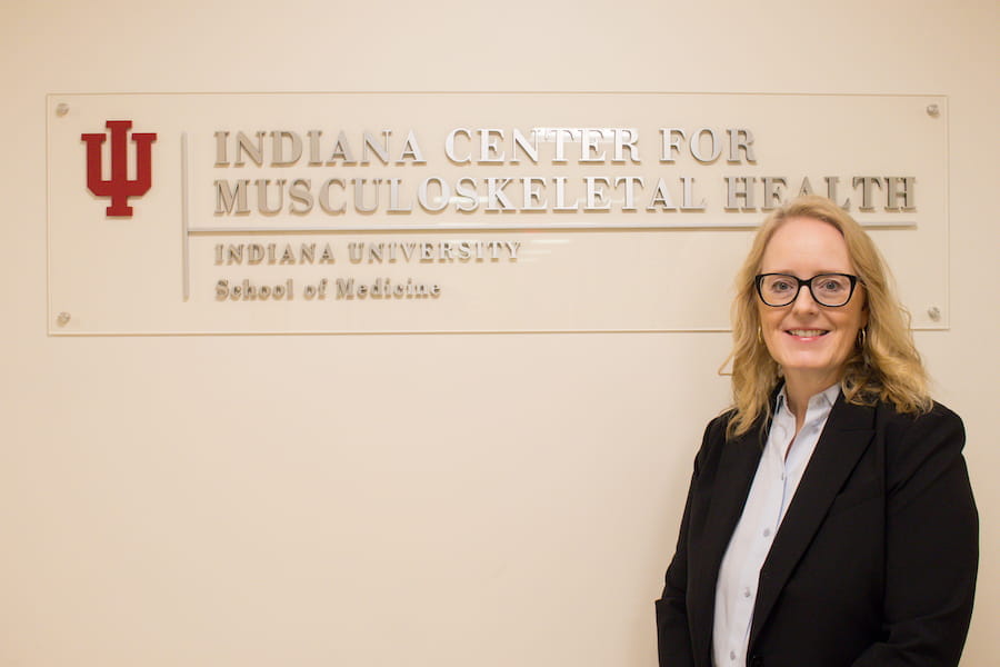 Melissa Kacena stands in front of the Indiana Center for Musculoskeletal Health sign, wearing a blouse and dark suit jacket
