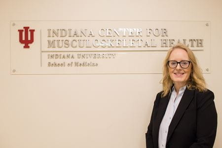 Melissa Kacena stands in front of the Indiana Center for Musculoskeletal Health sign, wearing a blouse and dark suit jacket