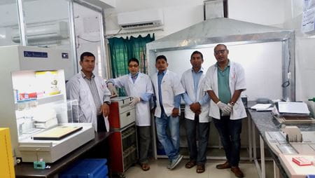 Five Nepalese men in laboratory coats stand inside the new histology lab at Lalgadh Leprosy Hospital in Nepal.