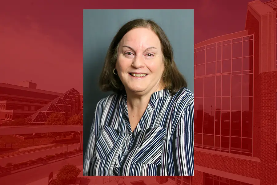 Headshot of Marlyn Baker wearing striped blouse on red campus building background