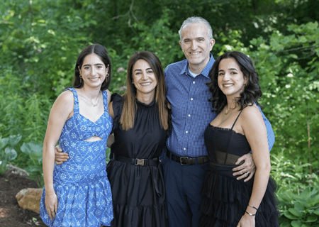 Zeina Nabhan poses outdoors with her two daughters and husband, all in dressy attire of blue and black.