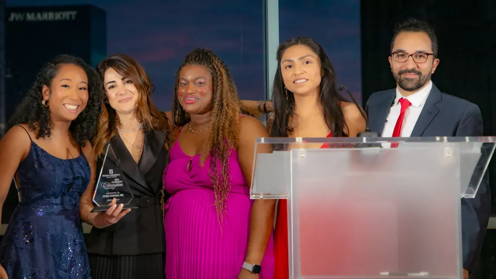 Zeina Nabhan, in black dress, holds a clear Diversity Champion award, stands near a podium with three women and one man with the Multicultural Physicians' Alliance.