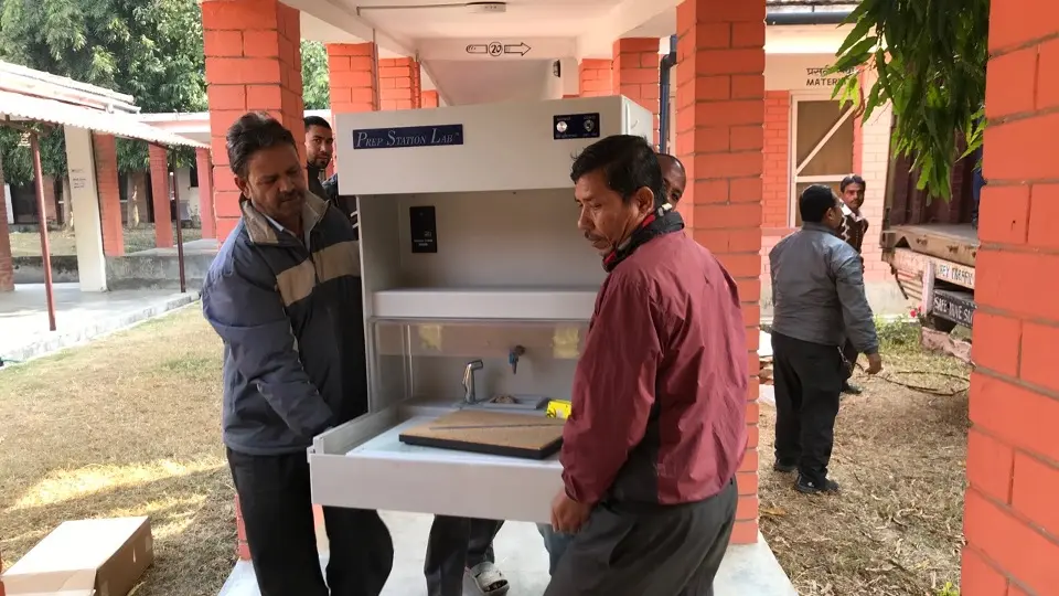 Two men carry laboratory equipment for a histology lab in Nepal.