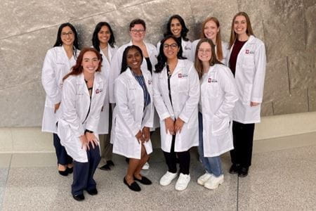 The 10 new residents stand in 2 rows outside of Walther Hall, wearing their IU School of Medicine white coats