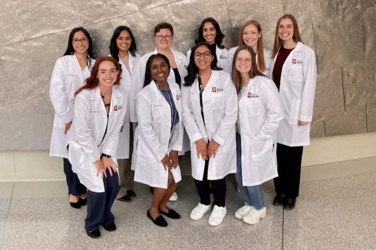 The 10 new residents stand in 2 rows outside of Walther Hall, wearing their IU School of Medicine white coats