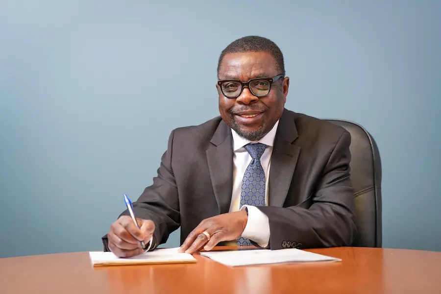 Kola Okuyemi sits at a desk with pen in hand