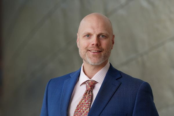 Headshot of Neil Perdue wearing blue suit jacket and red patterned tie