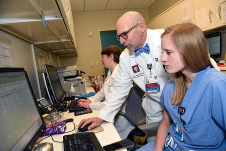 Dr. Peipert leans over a female resident's desk to work on a computer during training
