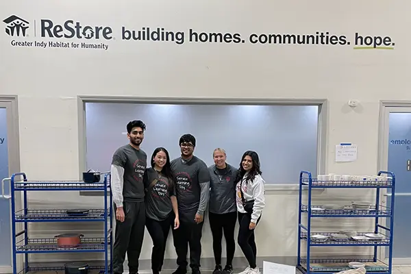 Five IU med students pose in front of a Habitat ReStore sign.