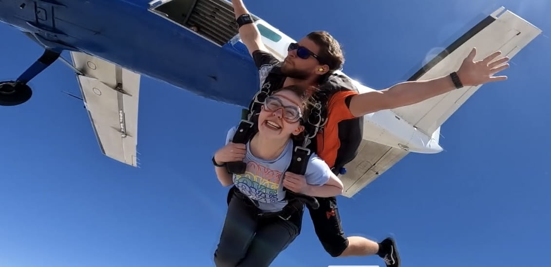 Sarah Vaught, stapped to a skydiver, smiling after jumping out of the airplane above