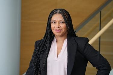 Tamika Dawson-Knox in light colored blouse with black jacket, standing in front of staircase in a medical school building