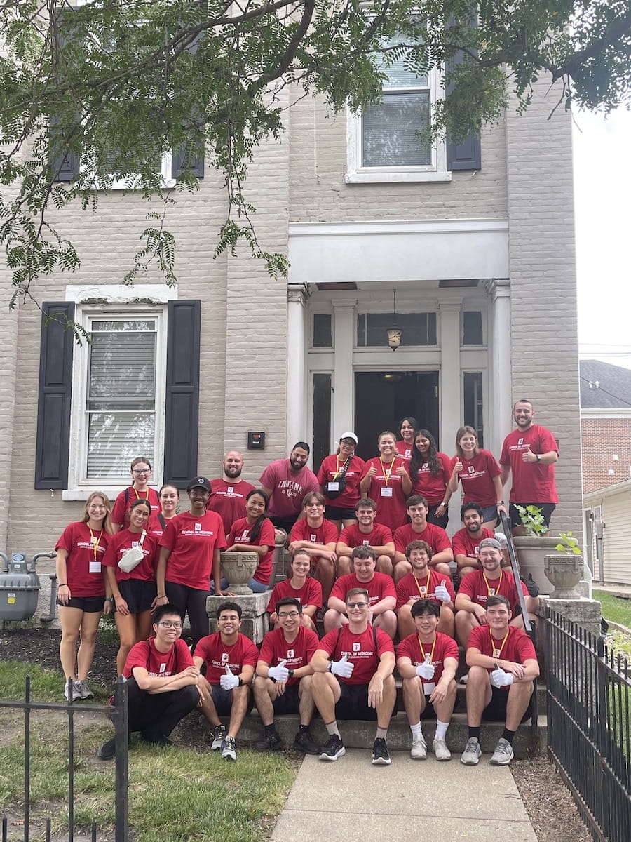 West Lafayette medical students in matching red shirts on a staircase at a Mental Health America apartment building where they volunteered during orientation week 2024.