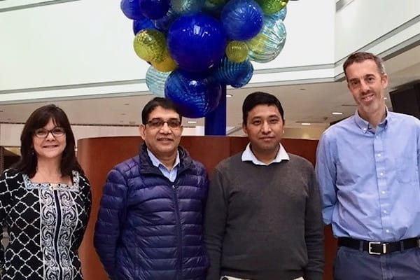 Debra Wood, Ravi Nepali, Krishna Bahadur Tamang and Simon Warren stand in front of the glass globe sculpture in the Med Sci Building.