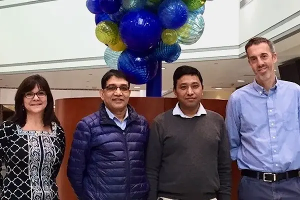 Debra Wood, Ravi Nepali, Krishna Bahadur Tamang and Simon Warren stand in front of the glass globe sculpture in the Med Sci Building.