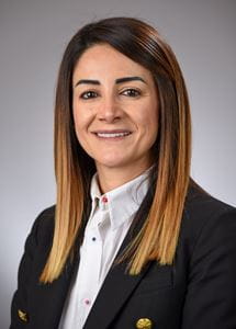 Zeina Nabhan professional headshot, woman with long brown hair wearing white button up and black coat