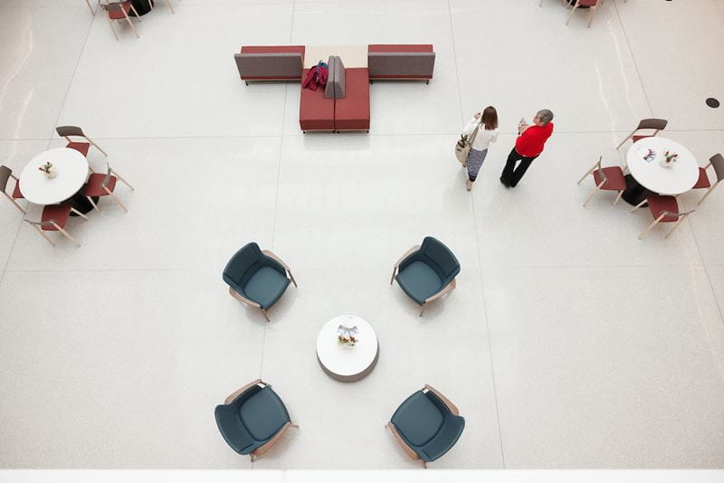 View of the Medical Education and Research Building atrium from above with two women walking by tables and chairs.