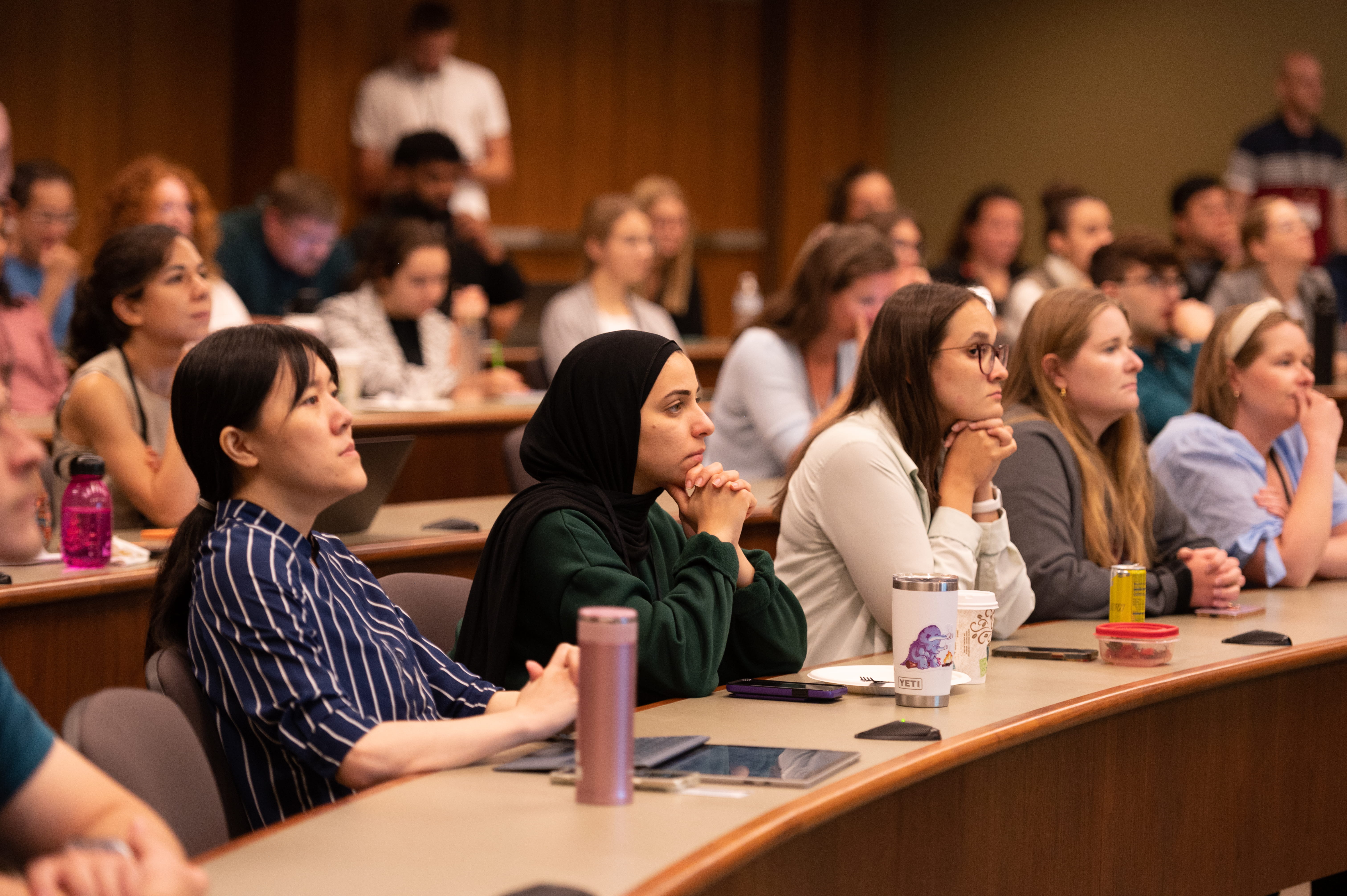 Audience member listen intently from seats behind long tables in an auditorium