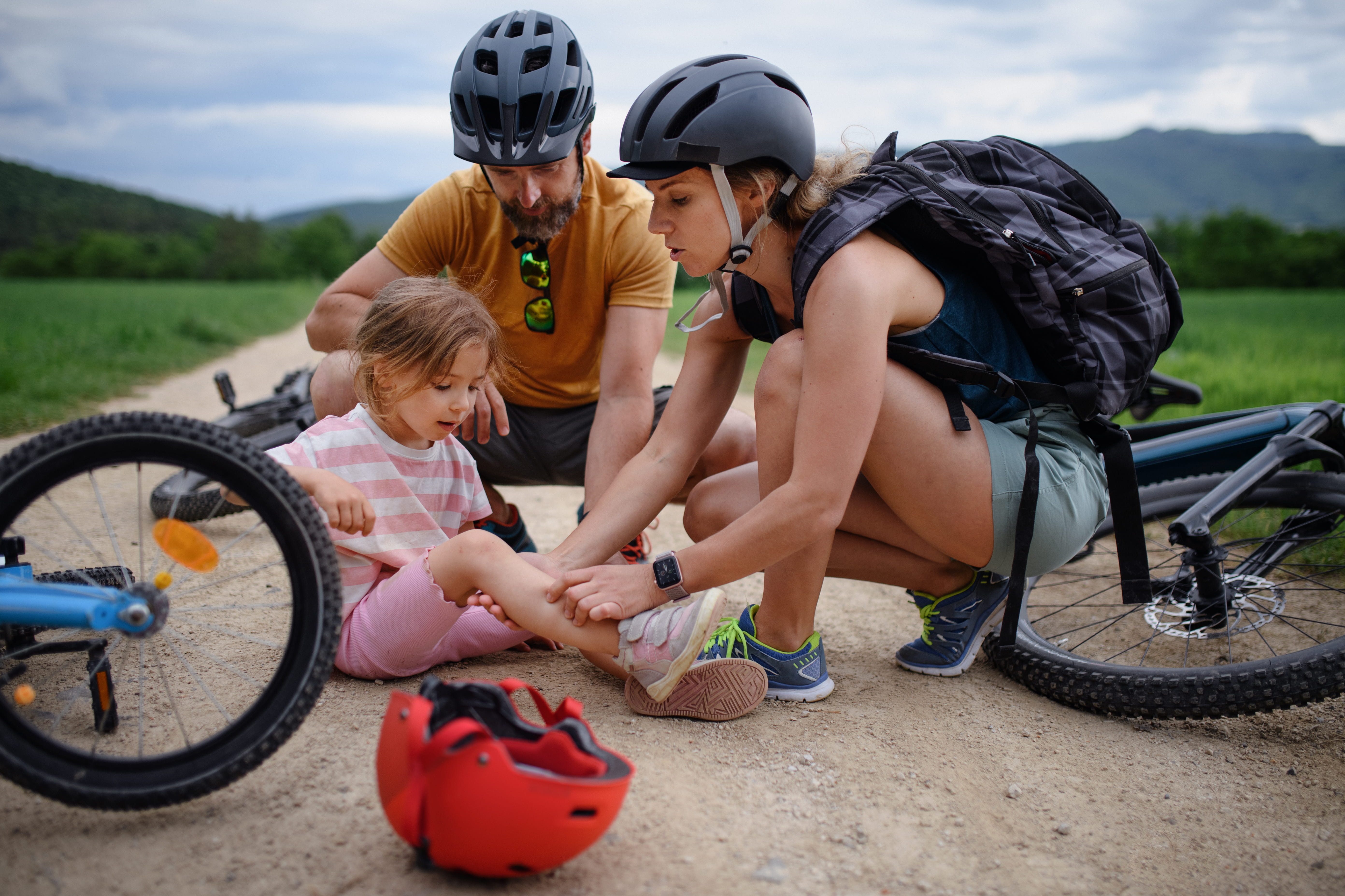 Dad and mom wearing bike helmets tend to little girl who fell off bike