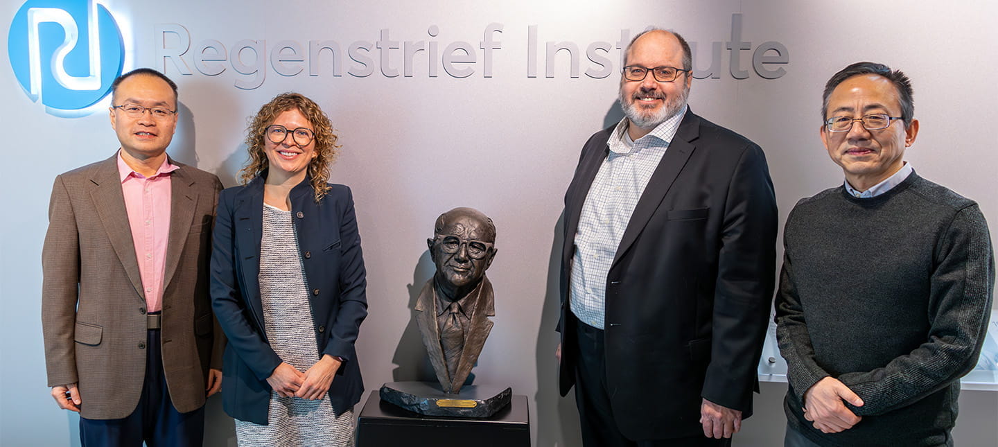 Four IU professors pose under the Regenstrief Institute logo, next to a bust of Sam Regenstrief. They are the smiling leaders of the AI in Healthcare Conference 2025