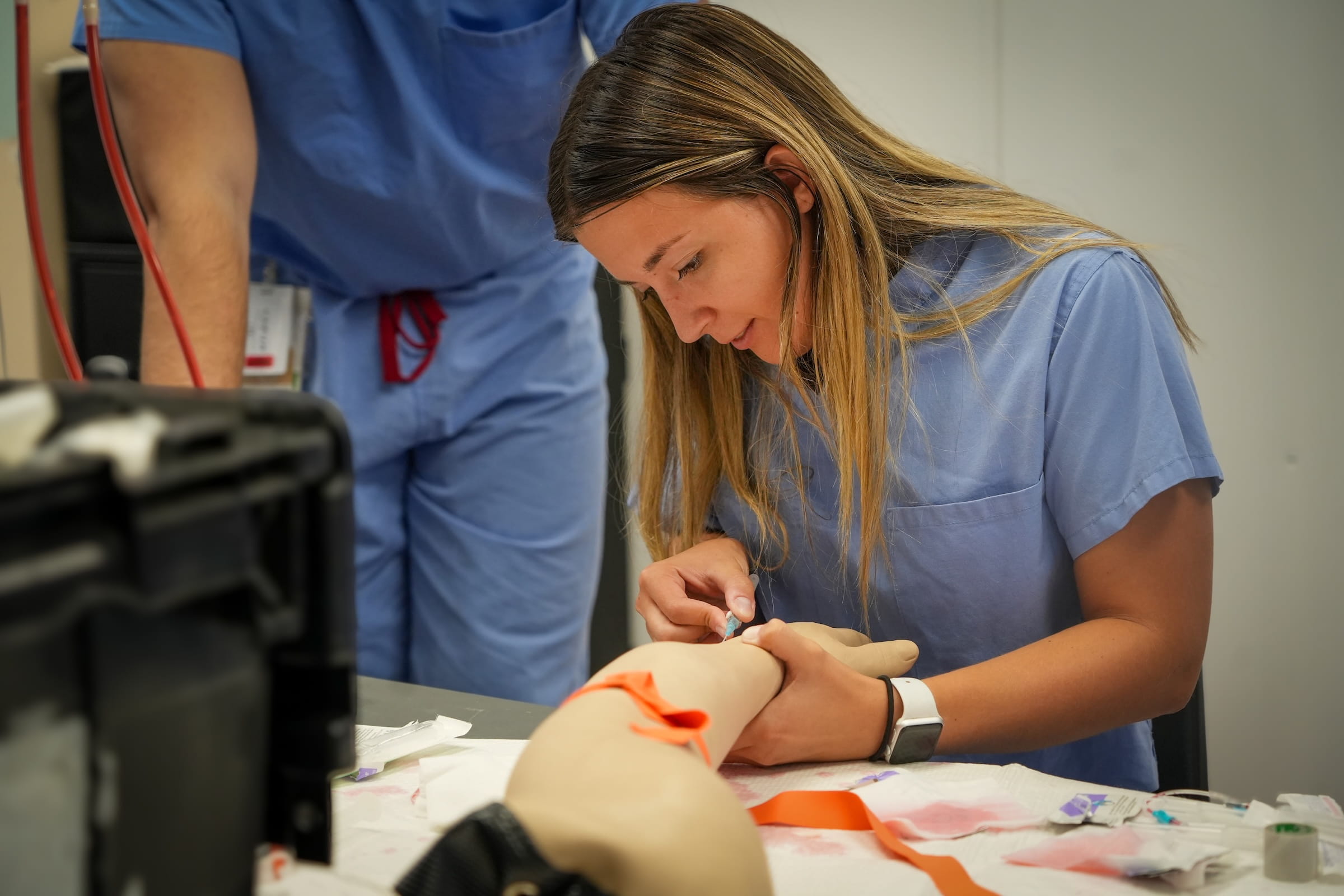 A female student practices placing an IV into a manikin arm.