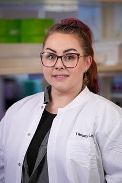Becky Wallings, woman with ponytail and glasses, wearing white coat with Tansey Lab logo