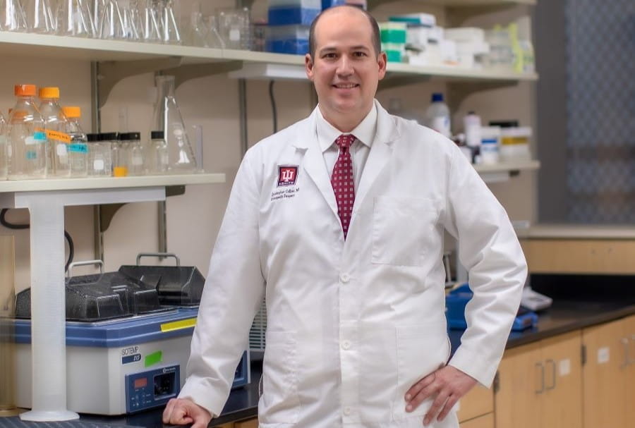 Christopher Collier stands in a laboratory and smiles. 