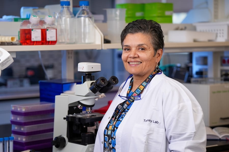 Malu Tansey, in white coat, poses in her research laboratory at IU School of Medicine.