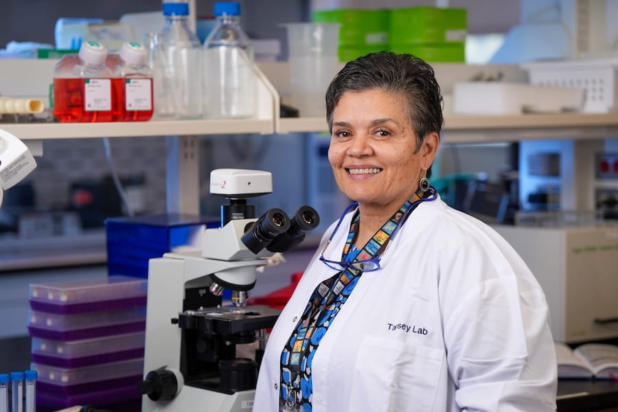 Malu Tansey, in white coat, poses in her research laboratory at IU School of Medicine.