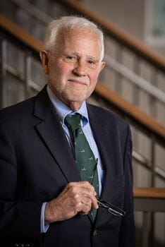 Portrait of Dr. Patrick R. O'Neil, wearing suit and tie and holding his glasses in hand