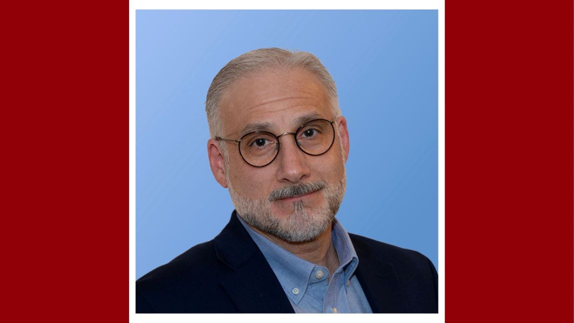 Headshot of a bearded man with short, gray hair wearing glasses and a suit.