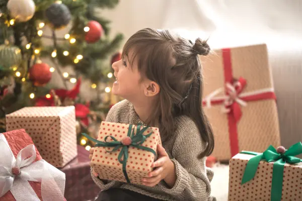 Little girl is holding a gift box and smiling while sitting at home. | Username - puhimec"