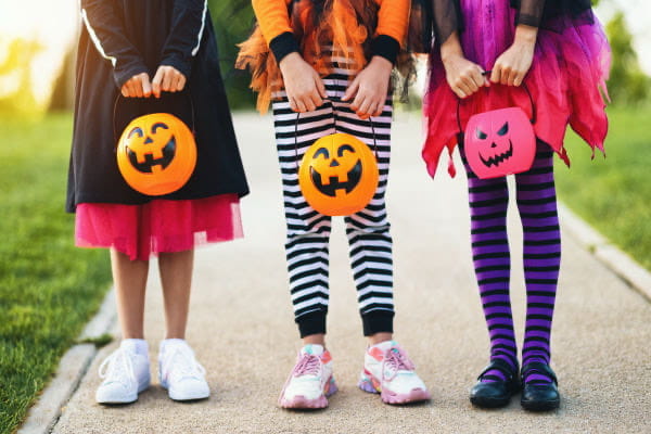 kids with Halloween costumes on and jack-o-lantern buckets to collect candy 