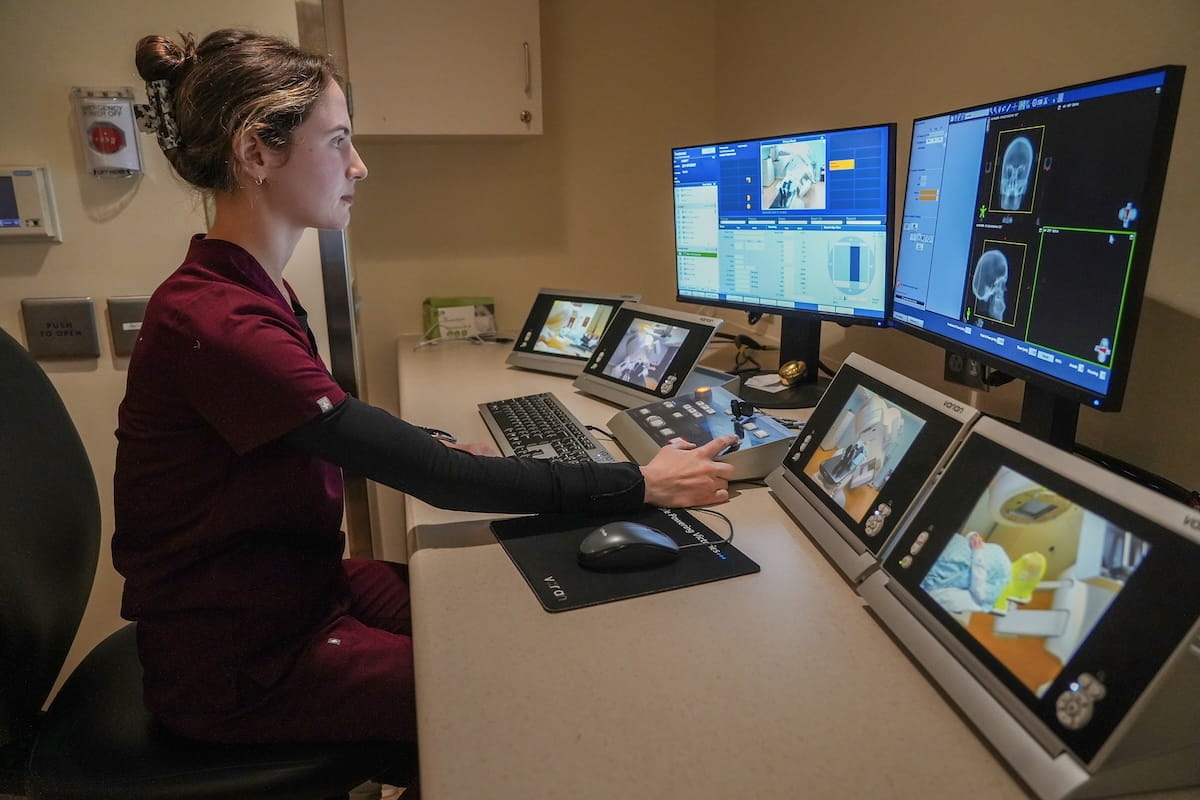 A student sits in front of multiple computer monitors for directing targeted radiation therapy.