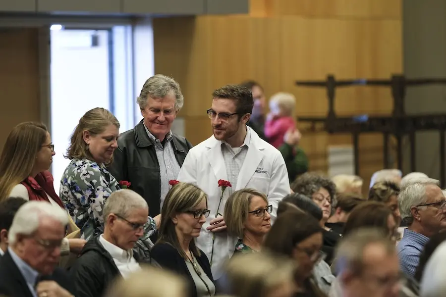 Man in white coat presents red carnations to people seated in IU Auditorium during Service of Gratitude.