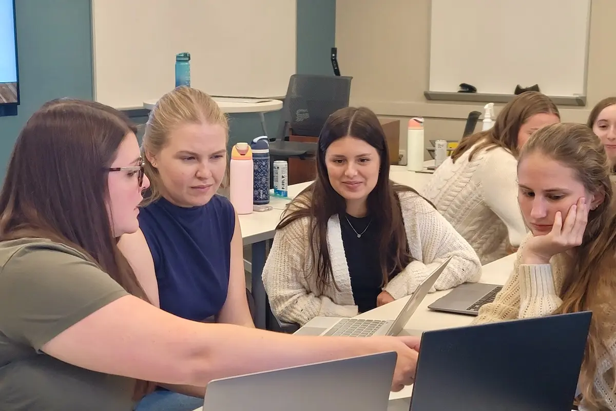 Genetic counseling students in a discussion group sitting with laptops at a table