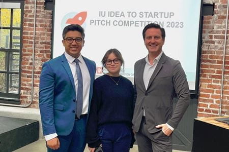 Sabin Karki and Brooke Stephanian stand with Dr. Gregory Borschel in front of a presentation screen at an IU Innovation pitch competition.
