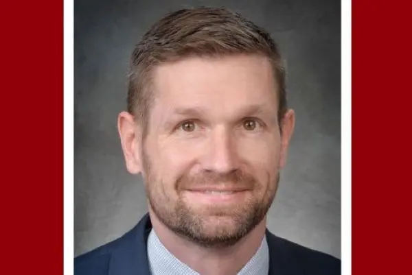 A headshot of John Leck, a man with short brown hair and a beard