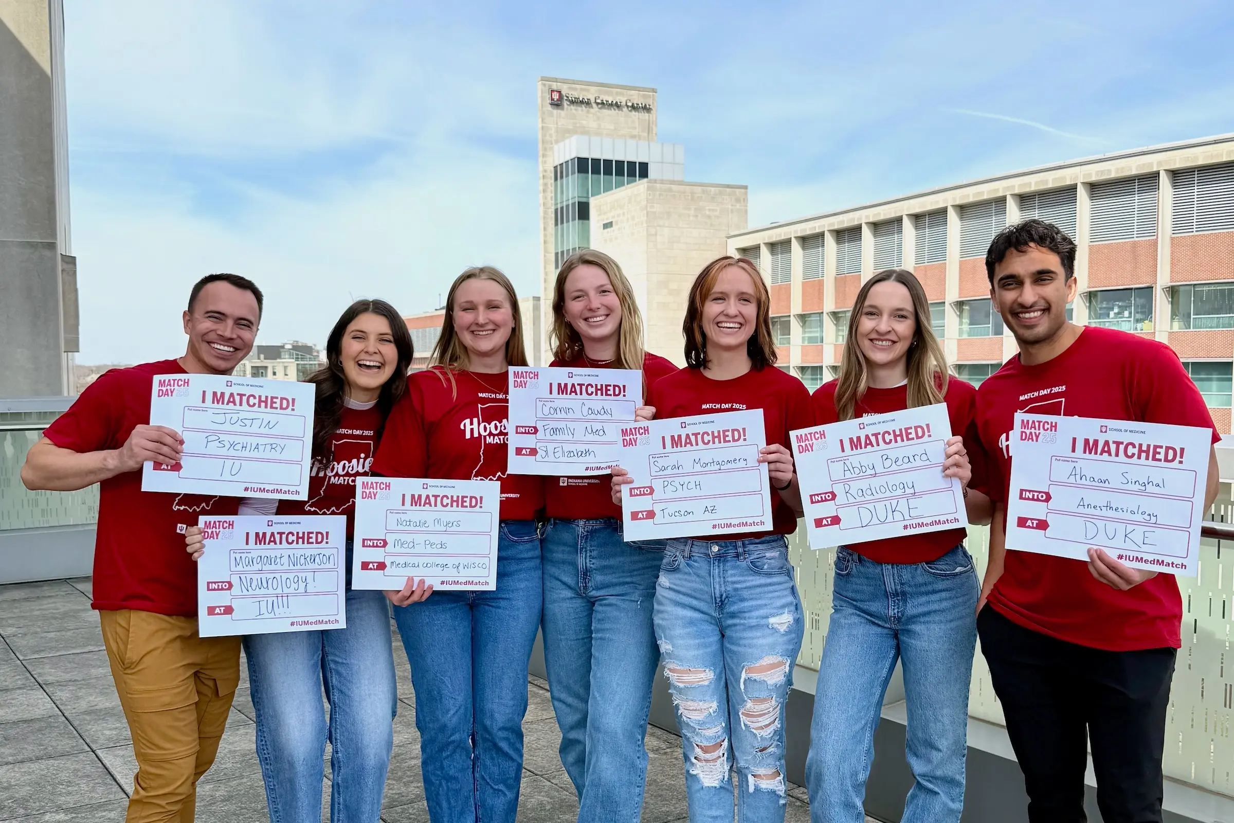Seven IUSM 2025 graduates hold Match Day signs listing their residency matches.