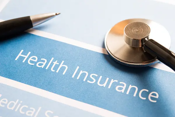 A pen and a stethoscope sit on a paper labeled "Health Insurance."