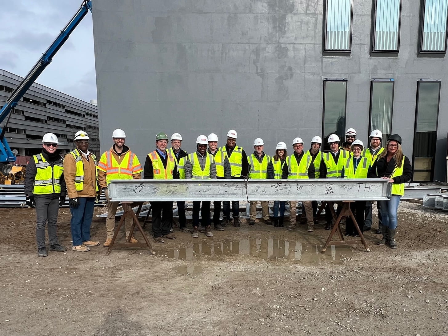 A group of construction planners in hardhats and orange vests pose with the last construction beam on the roof of the new Medical Education and Research Building.