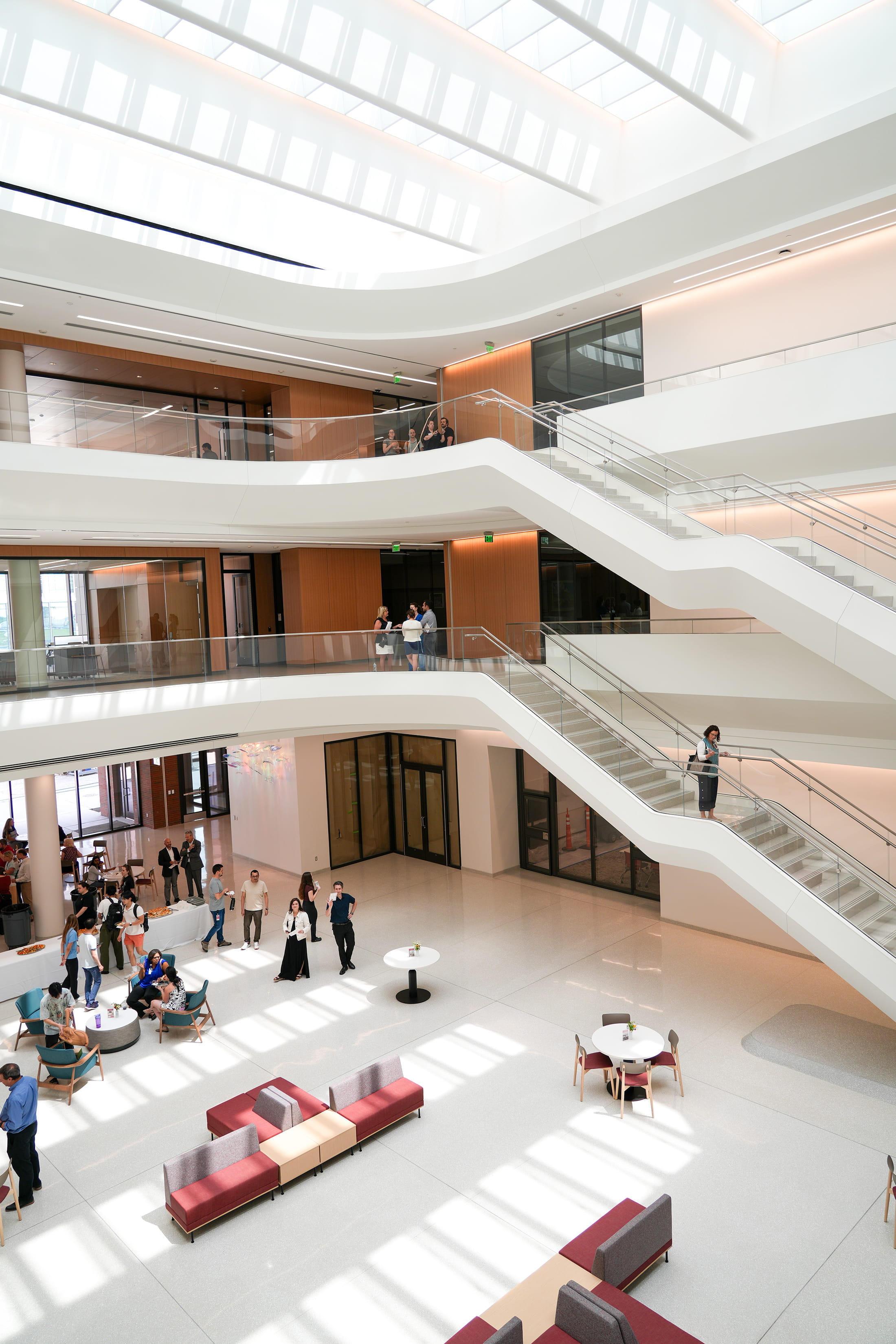 The Medical Education and Research Building atrium, from top floor window light to ground floor furnishings, with people walking on multi-level staircases and gathering below