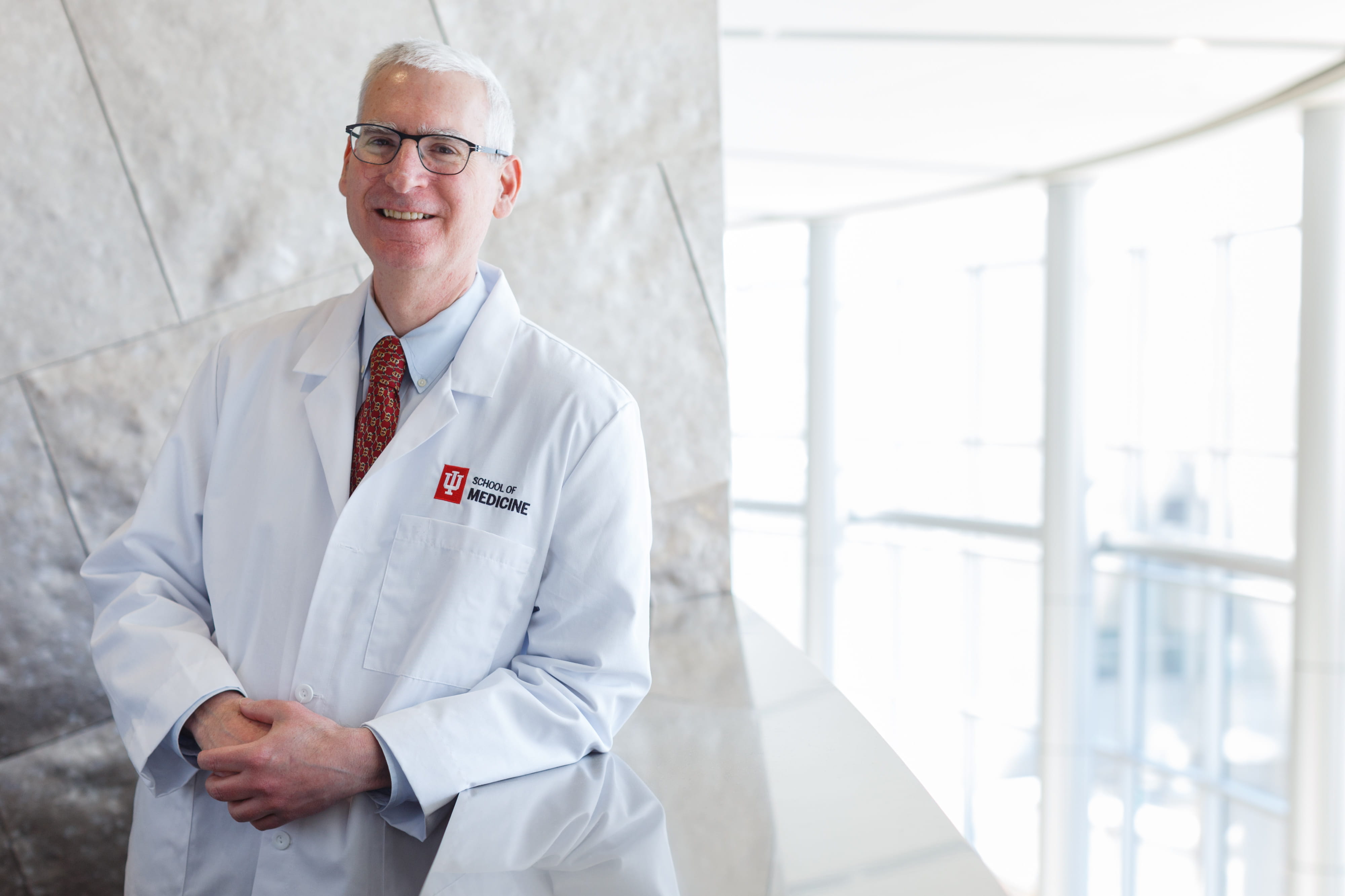 A man in a white lab coat poses on a stairwell. 