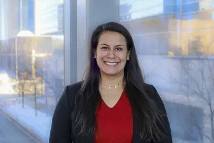 Michelle Miller head-and-shoulders portrait, wearing red top and black blazer, in front of window overlooking campus