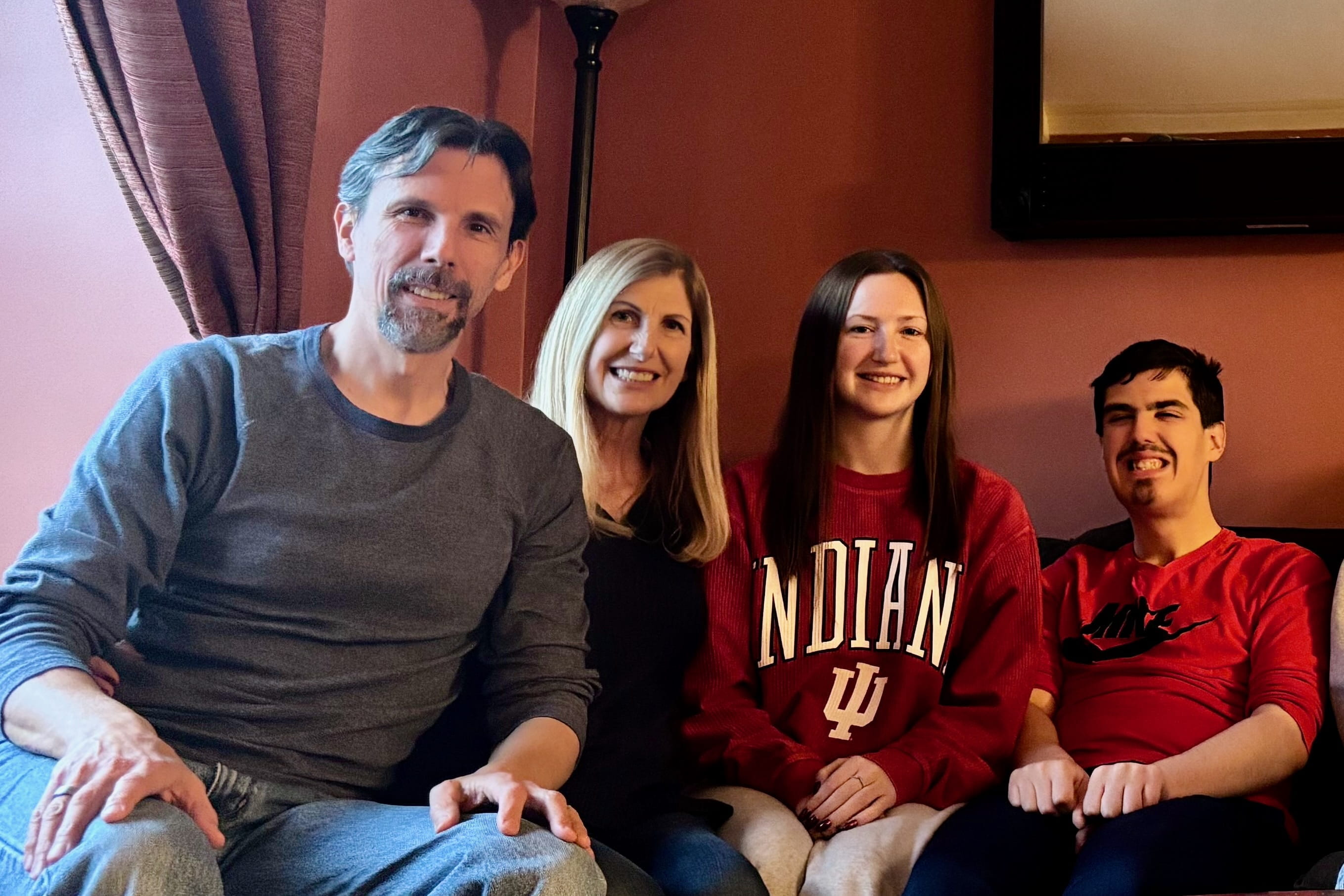 Molly Mizenko, wearing an IU sweatshirt, sits on a couch with her parents and brother