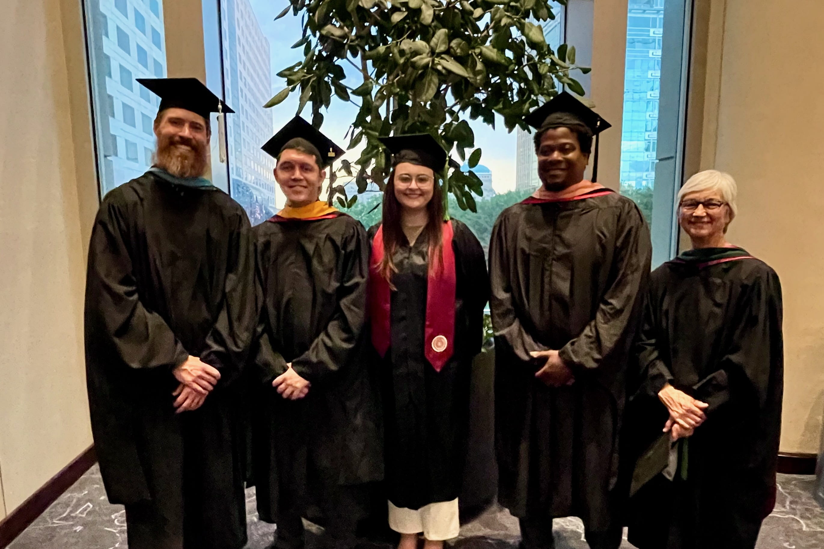 Jada Paul, in cap and gown, stands in the middle of a group of MLS faculty, all wearing graduation regalia