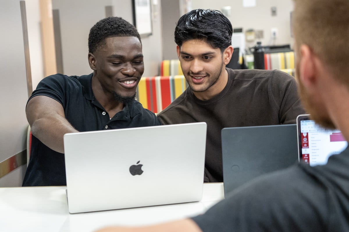IU medical students Mout-Maine Moustapha, Imran Hussein and Nathan Richardson sit at a table with laptops open as Moustapha points at the screen.