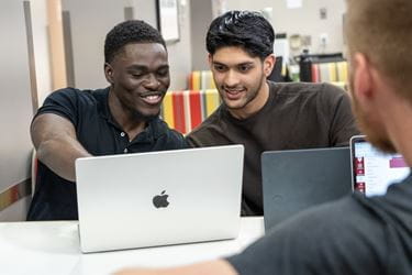 IU medical students Mout-Maine Moustapha, Imran Hussein and Nathan Richardson sit at a table with laptops open as Moustapha points at the screen.
