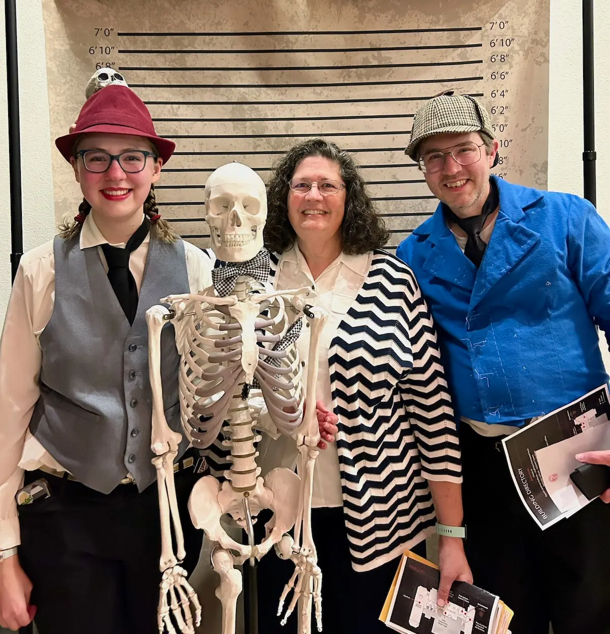Sarah Vaught and her parents, wearing detective costumes, posing with a skeleton