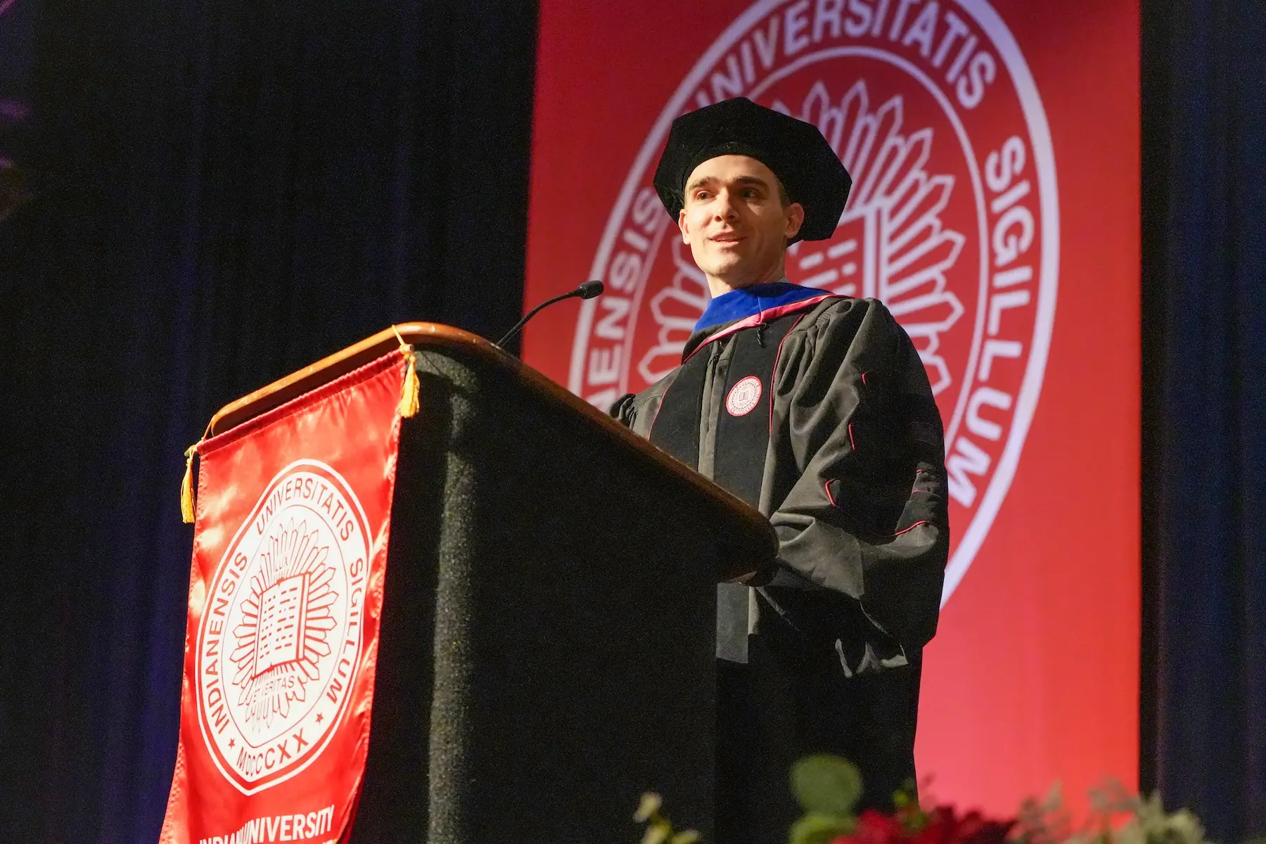 Oliver Strobel speaks from the podium at graduation, wearing his graduation regalia